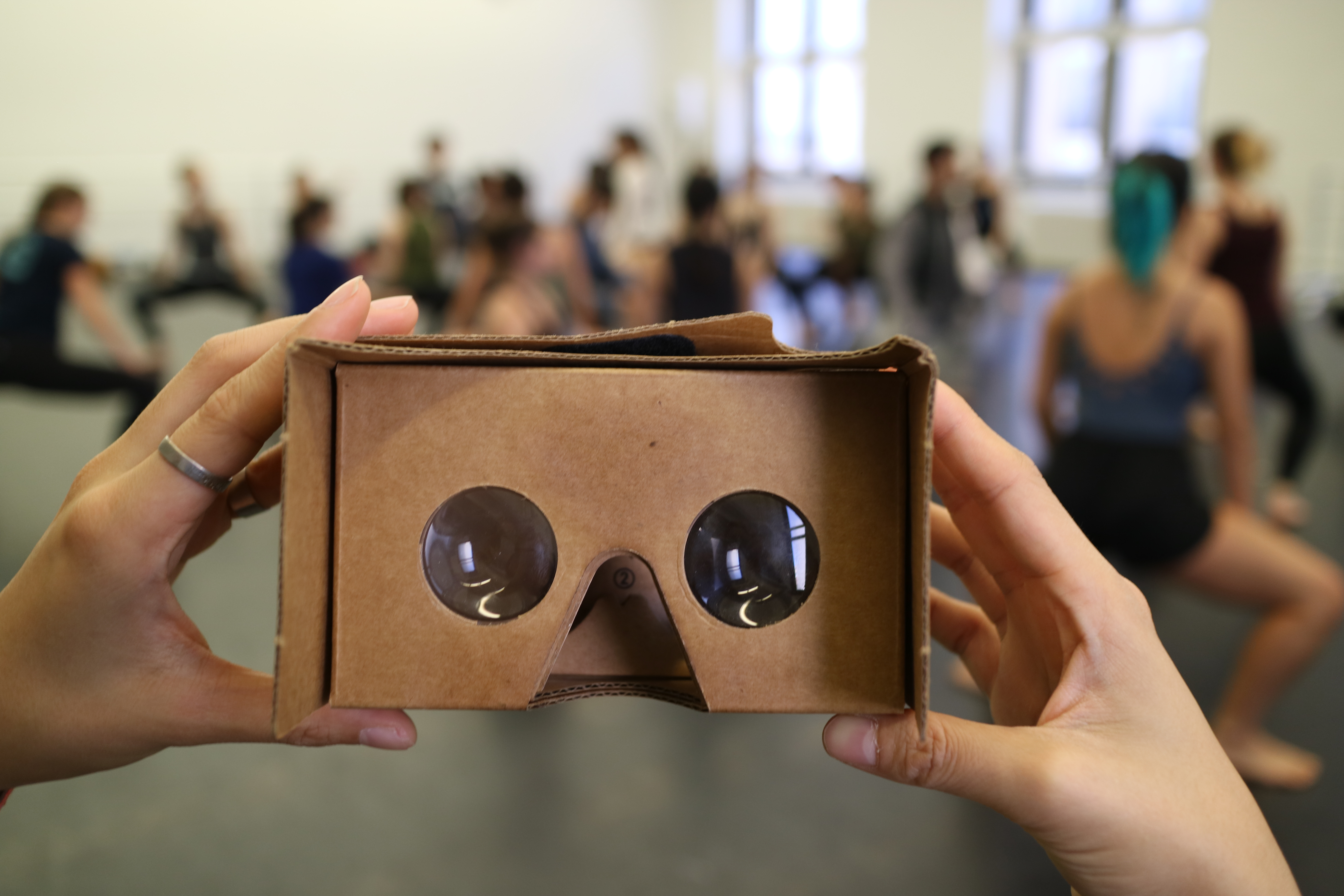 360 cardboard viewer is held in the foreground of dancers. 